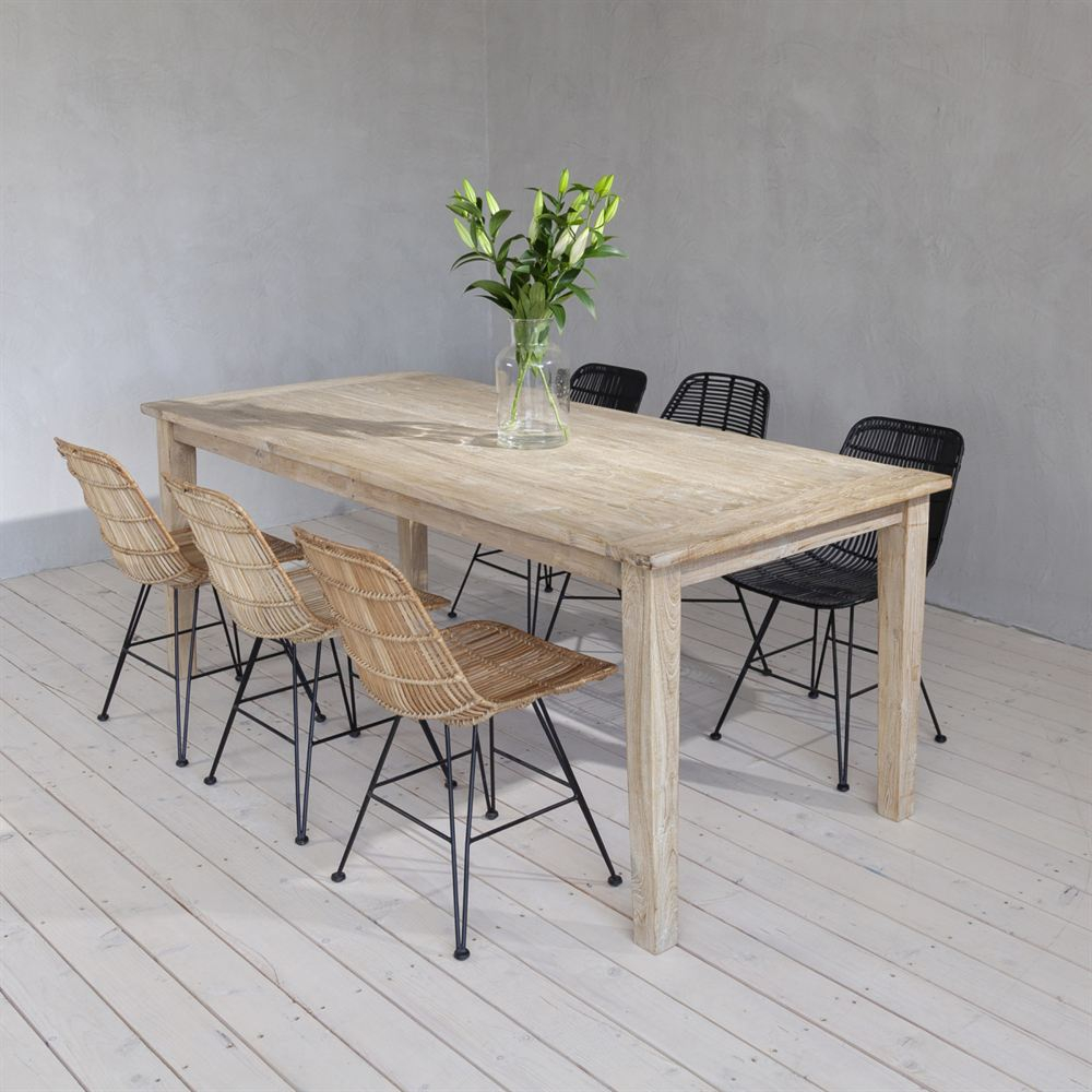 Heller Esstisch aus recyceltem Teak im Whitewash-Look mit Rattanstühlen und schwarzen Flechtstühlen, darauf eine Vase mit Lilien